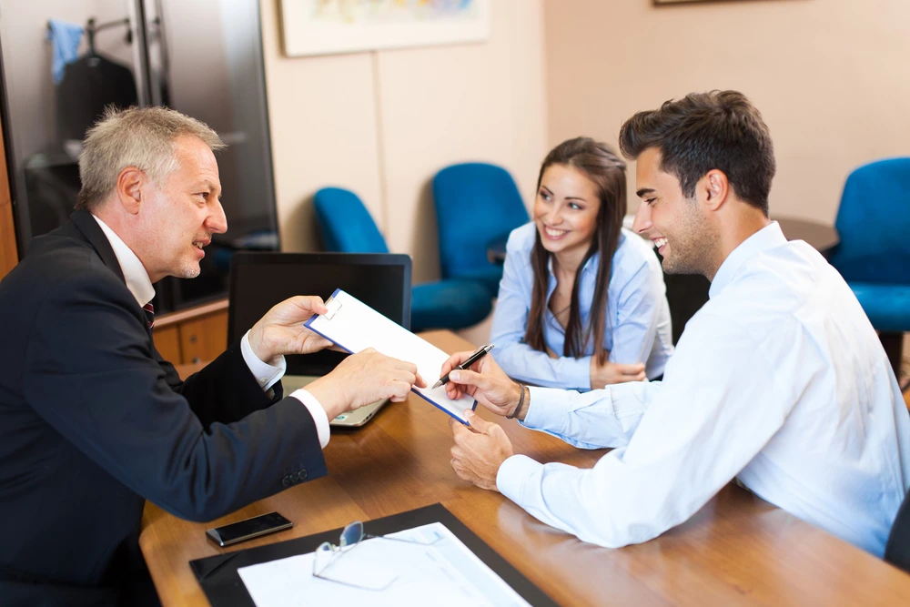 Advogado sentado em sua mesa, com um casal ao seu lado assinando um contrato de união estável